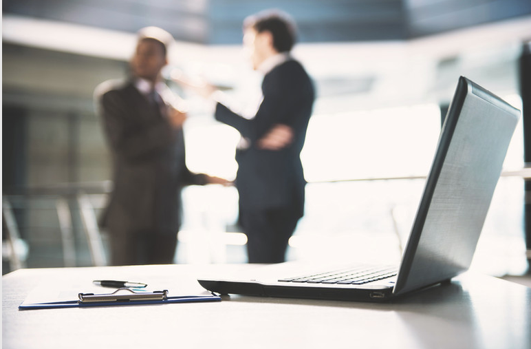Laptop and documents with business professionals talking in the background