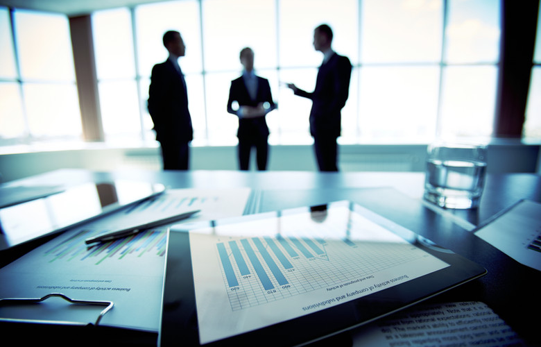 Business reports on a boardroom table with advisors in the background
